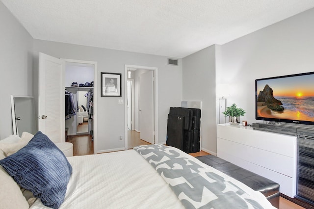 bedroom featuring a walk in closet, a closet, light hardwood / wood-style floors, and a textured ceiling