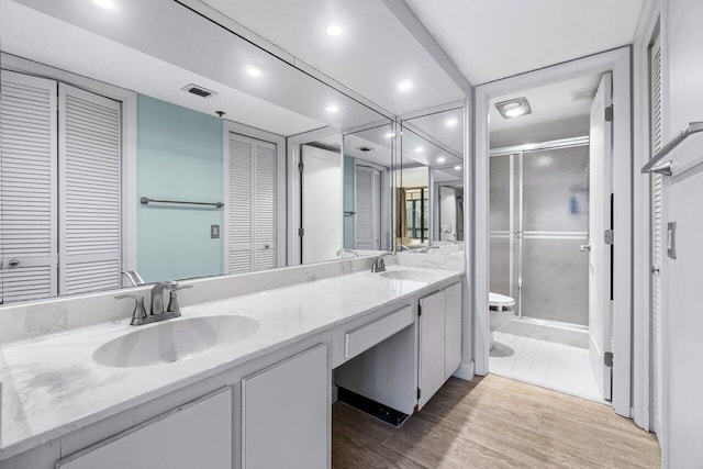 bathroom with wood-type flooring, vanity, toilet, and a shower with door