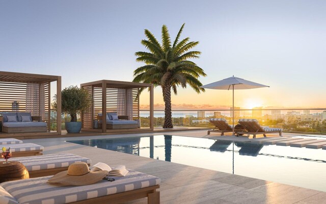 pool at dusk with a patio, a water view, and an outdoor pool