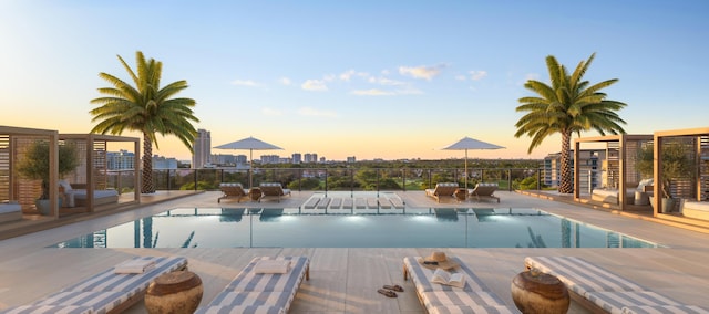 pool at dusk featuring a patio area, a city view, and a community pool