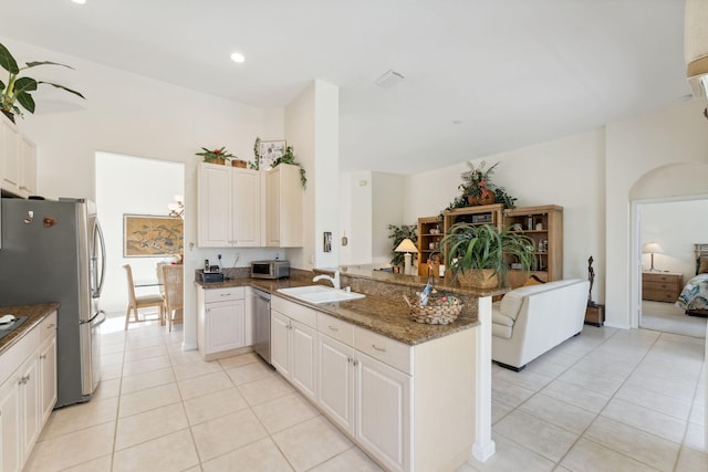 kitchen featuring sink, stainless steel appliances, dark stone countertops, light tile patterned floors, and kitchen peninsula