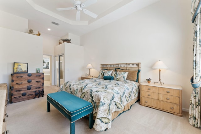 bedroom with ceiling fan, light colored carpet, a closet, and a tray ceiling