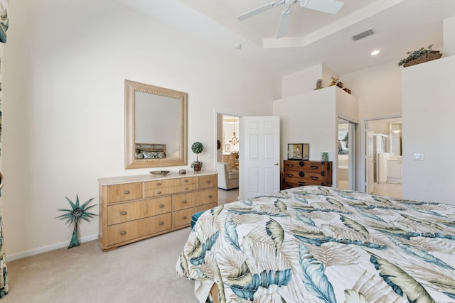 bedroom with connected bathroom, a towering ceiling, light colored carpet, a tray ceiling, and ceiling fan