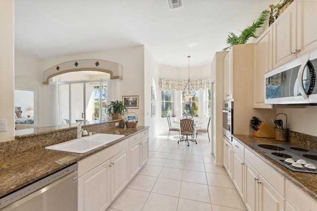 kitchen with sink, appliances with stainless steel finishes, light tile patterned flooring, decorative light fixtures, and dark stone counters