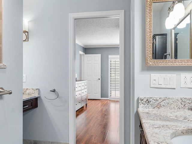 bathroom featuring hardwood / wood-style floors, vanity, crown molding, and a textured ceiling