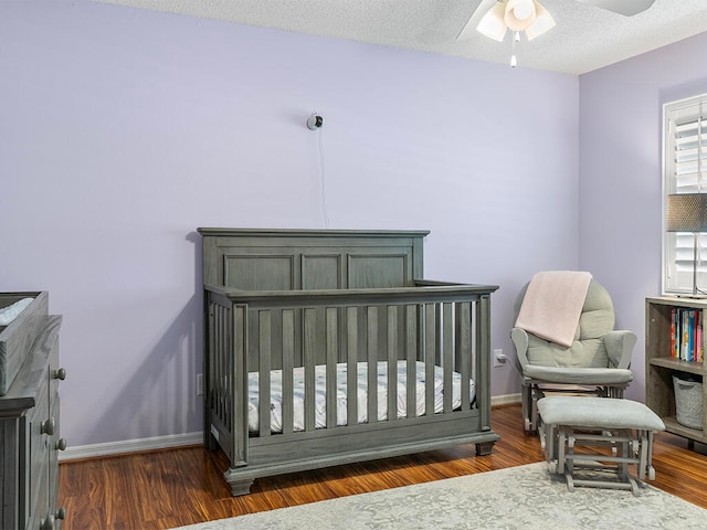 bedroom featuring ceiling fan, dark wood-type flooring, a nursery area, and a textured ceiling