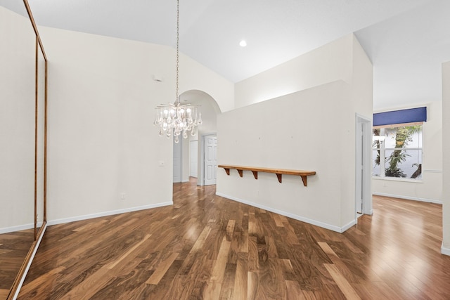 unfurnished living room with high vaulted ceiling, dark wood-type flooring, and a notable chandelier