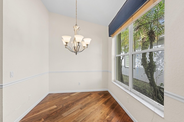 spare room featuring hardwood / wood-style flooring, vaulted ceiling, a wealth of natural light, and an inviting chandelier