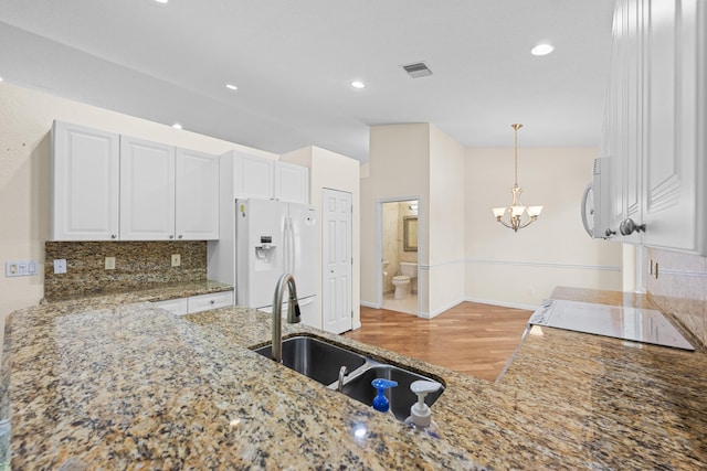 kitchen with white appliances, tasteful backsplash, white cabinetry, and a notable chandelier