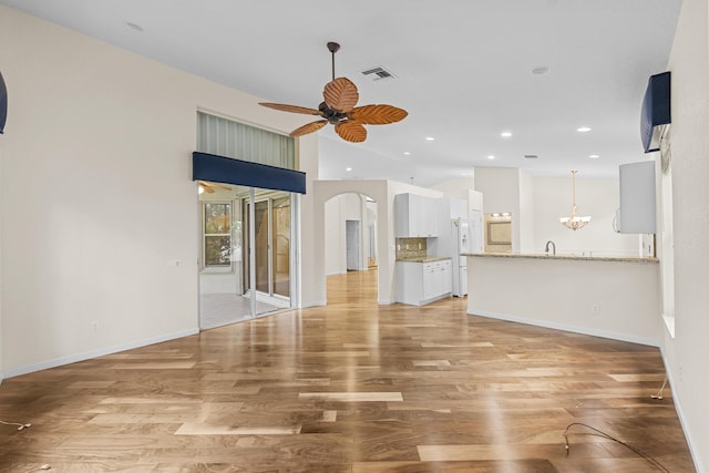 unfurnished living room featuring ceiling fan with notable chandelier, light wood-type flooring, and lofted ceiling