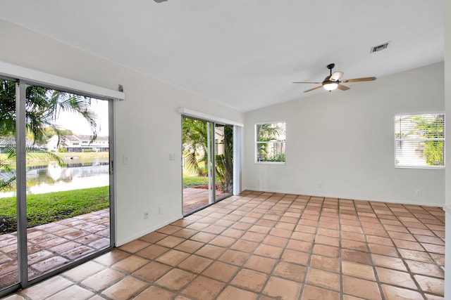 empty room featuring light tile patterned floors, a water view, ceiling fan, and a healthy amount of sunlight