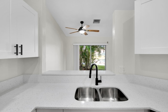 interior details featuring white cabinets, light stone counters, ceiling fan, and sink