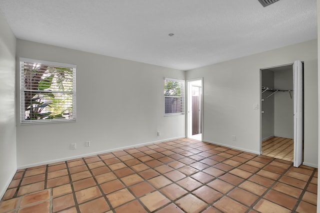 unfurnished bedroom with tile patterned flooring, a walk in closet, a textured ceiling, and a closet