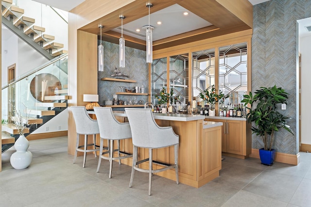 bar featuring a raised ceiling, light brown cabinets, and pendant lighting