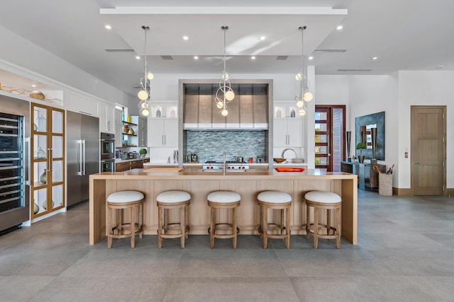 kitchen featuring white cabinetry, a kitchen breakfast bar, backsplash, hanging light fixtures, and a large island