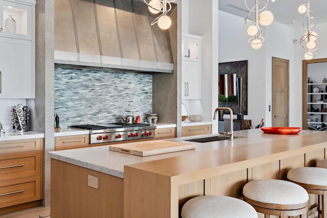 kitchen with an island with sink, tasteful backsplash, range hood, white cabinets, and sink