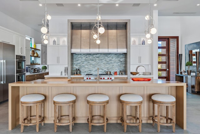 kitchen featuring high quality fridge, white cabinetry, backsplash, a large island, and a breakfast bar area