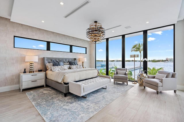 bedroom featuring floor to ceiling windows, a chandelier, a water view, and light wood-type flooring