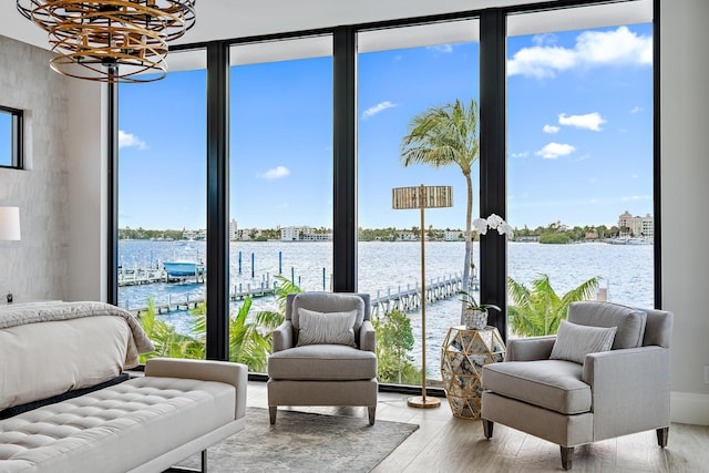 bedroom with a wall of windows, light wood-type flooring, a water view, and an inviting chandelier