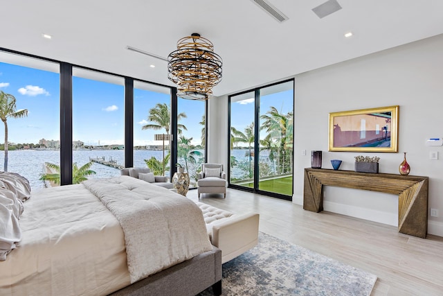 bedroom featuring light wood-type flooring, access to exterior, a chandelier, a water view, and expansive windows