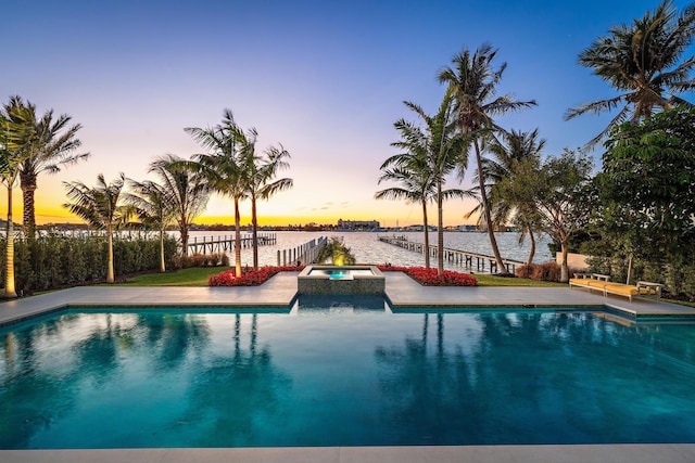 pool at dusk featuring a water view and an in ground hot tub