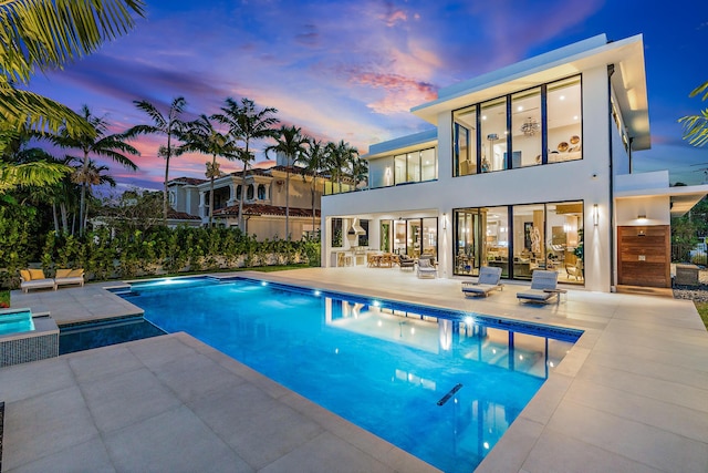 pool at dusk with a jacuzzi and a patio