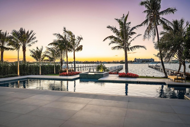 pool at dusk featuring an in ground hot tub and a water view