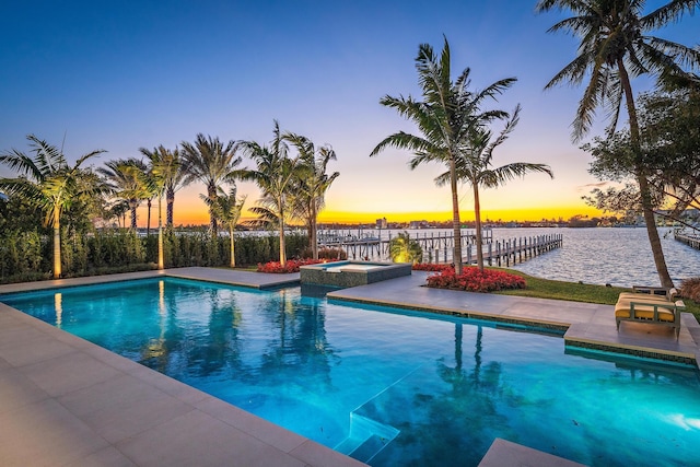 pool at dusk featuring a water view and an in ground hot tub