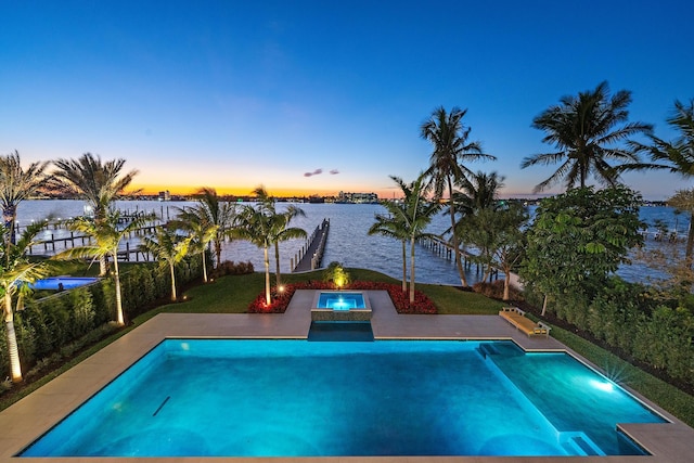 pool at dusk featuring a water view and an in ground hot tub