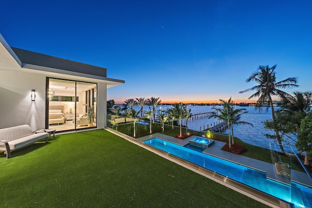 pool at dusk featuring a water view and a lawn