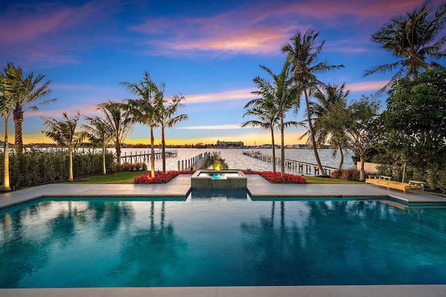 pool at dusk with a water view and an in ground hot tub