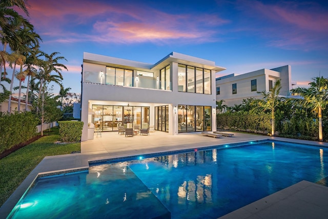 back house at dusk featuring a fenced in pool and a patio area