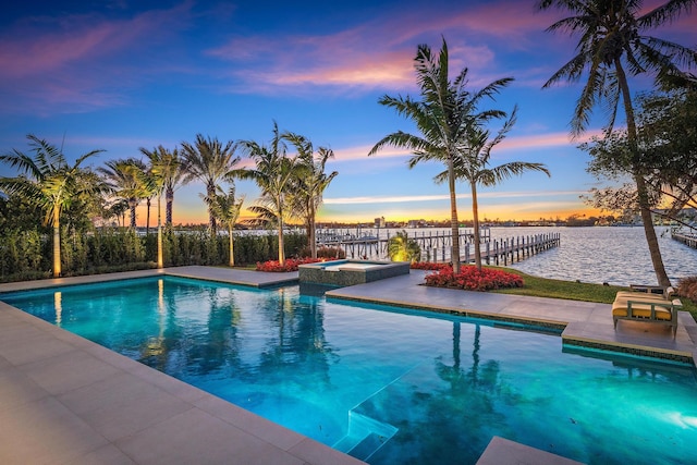 pool at dusk with an in ground hot tub and a water view