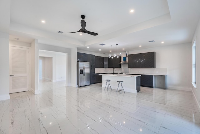 kitchen with a kitchen island with sink, ceiling fan, stainless steel fridge, a kitchen bar, and extractor fan