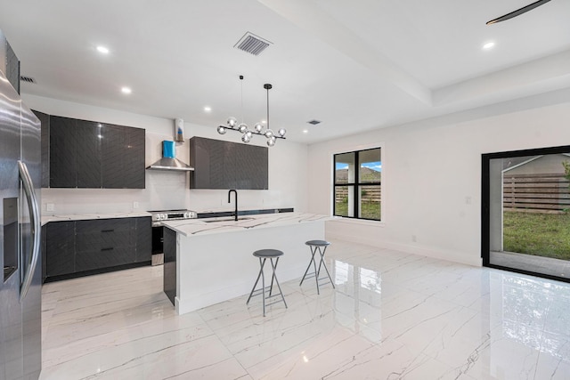 kitchen featuring a kitchen island with sink, a kitchen breakfast bar, wall chimney range hood, sink, and hanging light fixtures