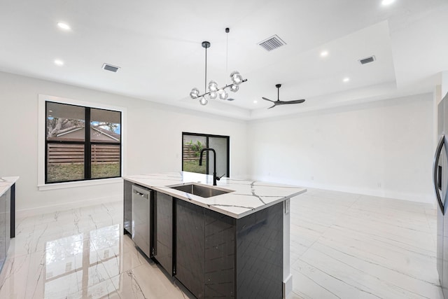 kitchen with sink, hanging light fixtures, light stone counters, a center island with sink, and ceiling fan with notable chandelier