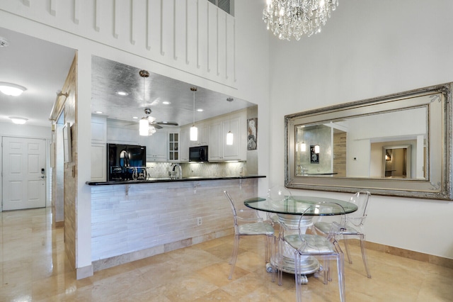 kitchen featuring a towering ceiling, ceiling fan with notable chandelier, black appliances, pendant lighting, and white cabinetry