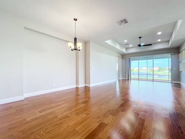 empty room with a raised ceiling, ceiling fan with notable chandelier, and light hardwood / wood-style flooring