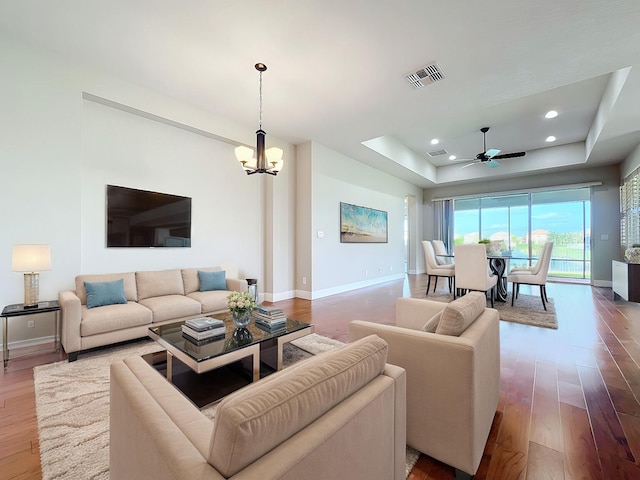 living room with hardwood / wood-style floors, ceiling fan with notable chandelier, and a tray ceiling