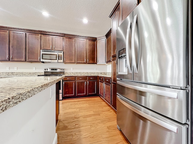 kitchen featuring light stone countertops, stainless steel appliances, a textured ceiling, and light wood-type flooring