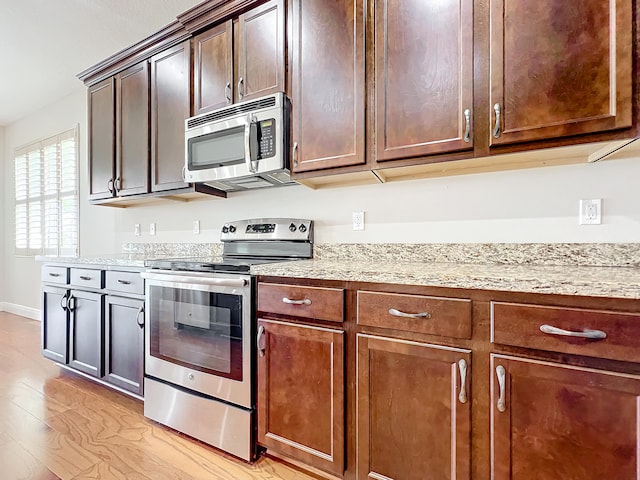 kitchen with light hardwood / wood-style floors, light stone counters, dark brown cabinetry, and appliances with stainless steel finishes