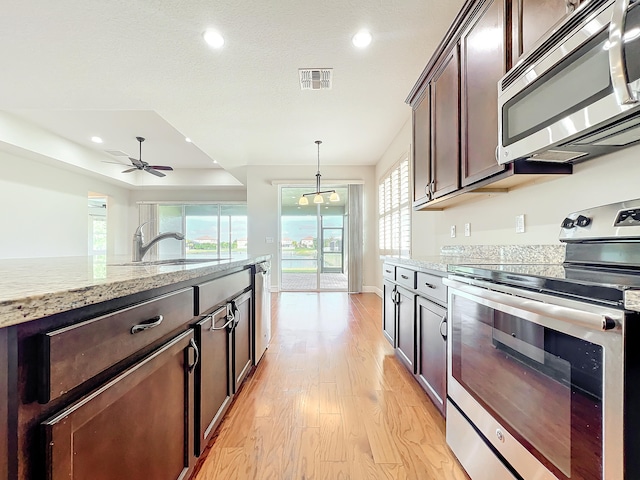 kitchen featuring dark brown cabinetry, ceiling fan, stainless steel appliances, light stone counters, and light wood-type flooring