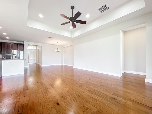 unfurnished living room with hardwood / wood-style floors, ceiling fan with notable chandelier, and a raised ceiling