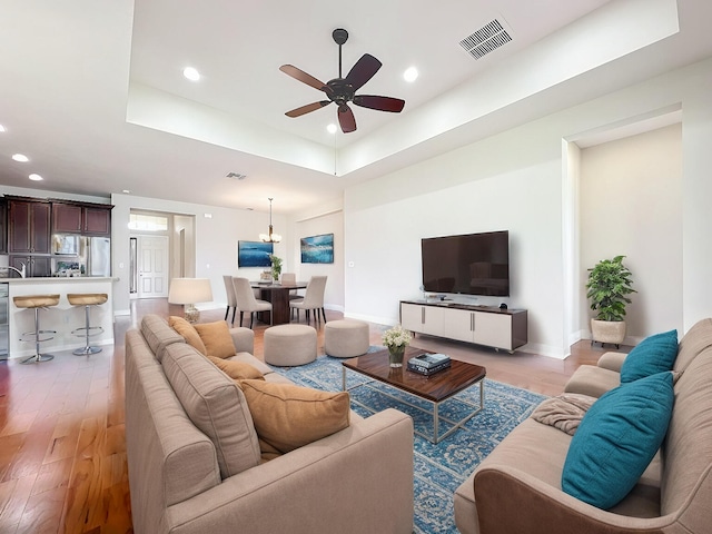 living room with a tray ceiling, ceiling fan, and light hardwood / wood-style flooring