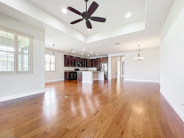 unfurnished living room with a raised ceiling, light hardwood / wood-style flooring, and ceiling fan with notable chandelier