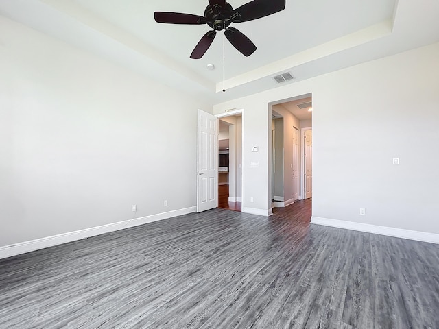 empty room with a raised ceiling, ceiling fan, and dark hardwood / wood-style flooring