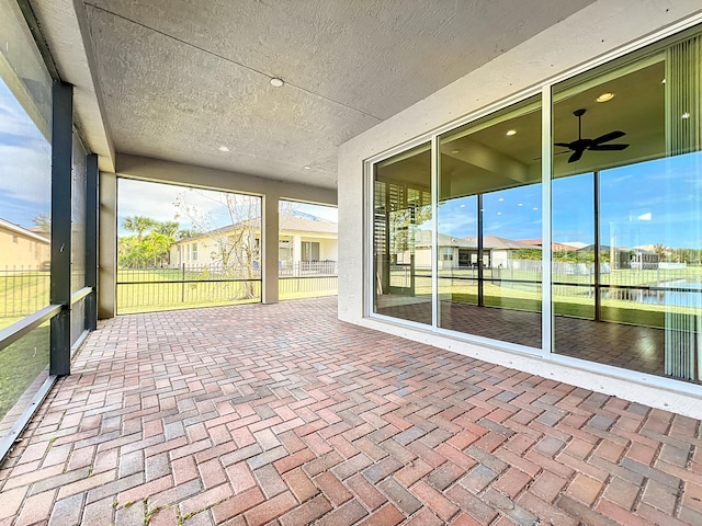 unfurnished sunroom featuring ceiling fan and a water view