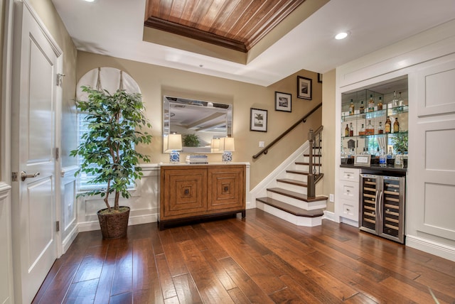 bar with a raised ceiling, beverage cooler, dark hardwood / wood-style floors, and ornamental molding