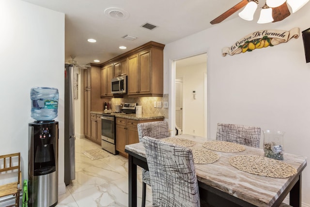 kitchen featuring light stone countertops, decorative backsplash, ceiling fan, and stainless steel appliances