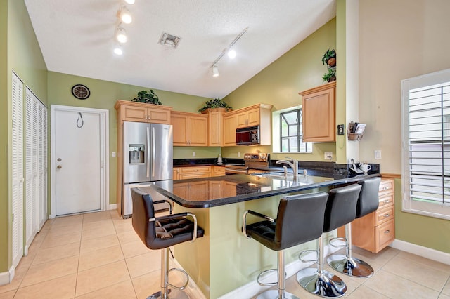 kitchen featuring a kitchen breakfast bar, kitchen peninsula, vaulted ceiling, light brown cabinetry, and appliances with stainless steel finishes